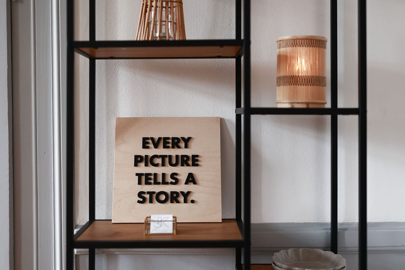 Holzschild auf einem Regal, mit dem Text "Every picture tells a story"