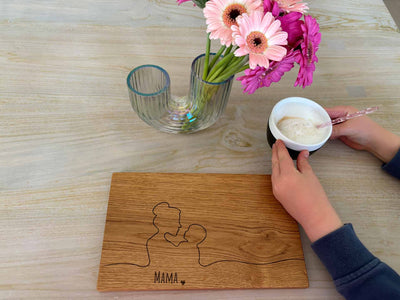 Mama Frühstücksbrettchen aus Holz auf einem Tisch mit Blumen und ein Kind greift nach einem Kaffee