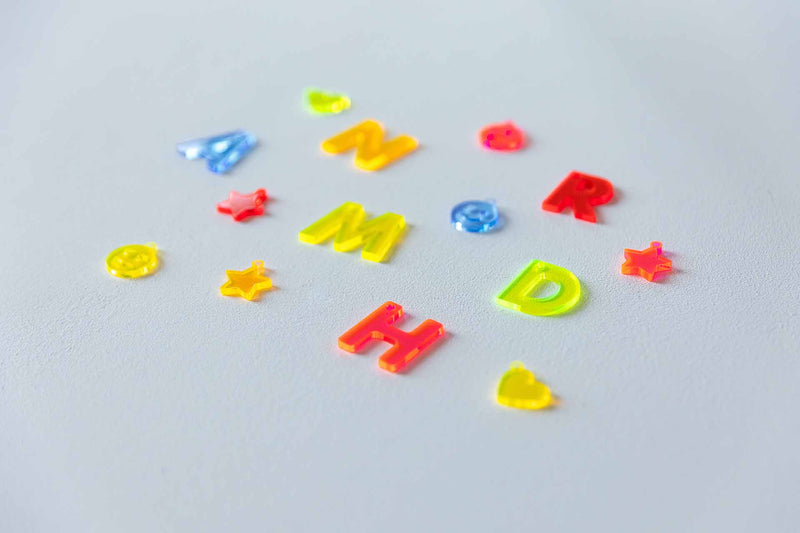 14 Neon-Acryl-Buchstaben und -Anhänger auf weißem Hintergrund, fotografiert von der Seite