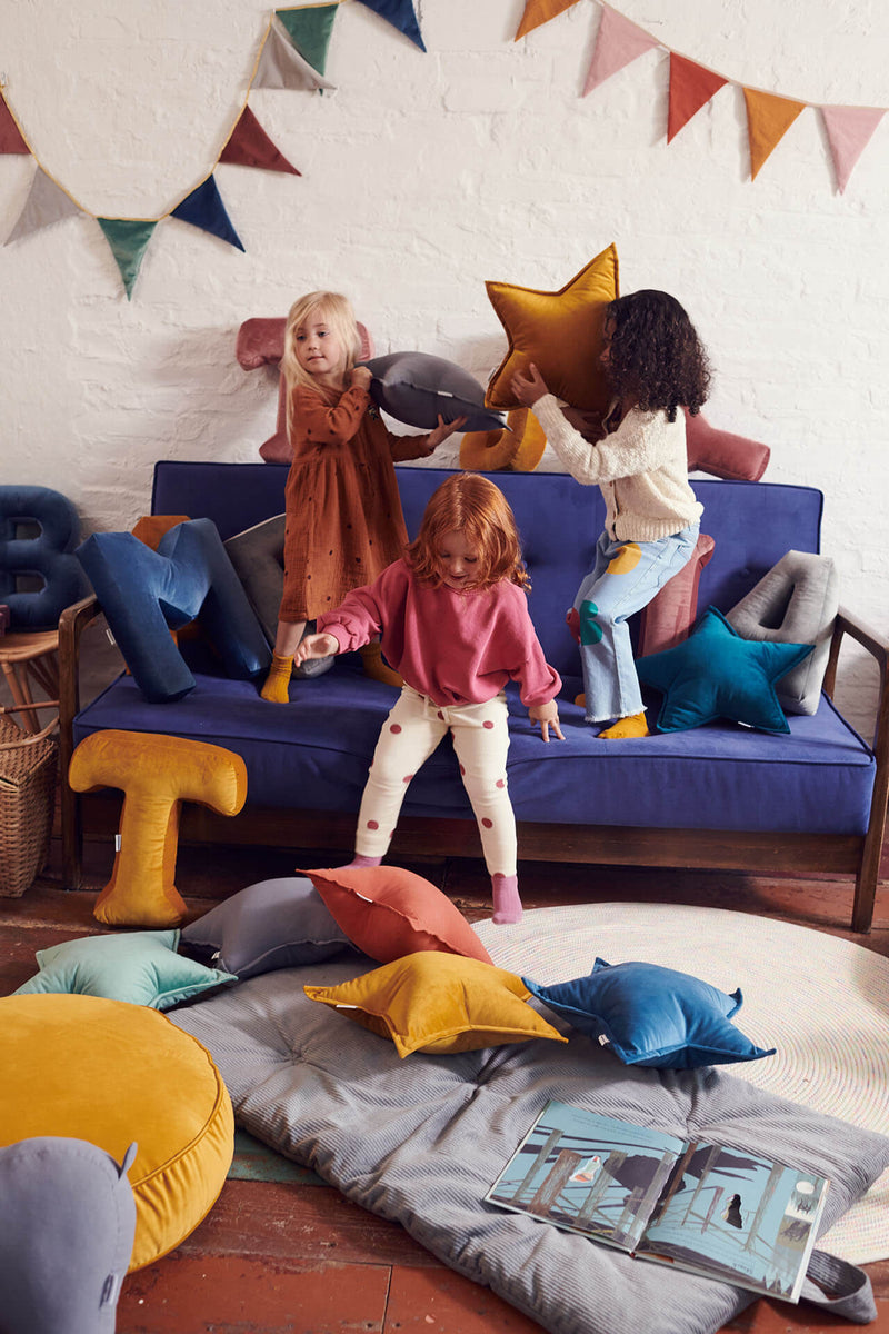 Kinder spielen im Wohnzimmer mit Samtkissen. Samtgirlanden hängend an der Wand.