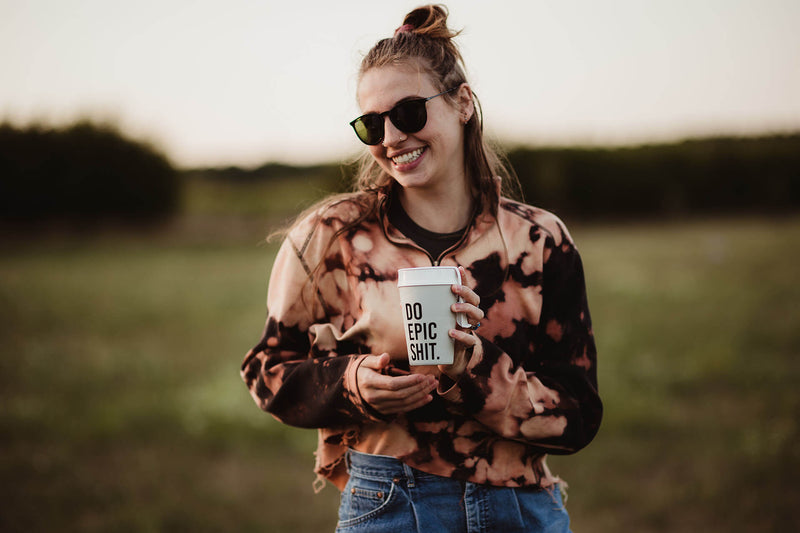 Junge Frau hält ein To Go Kaffeebecher, wo drauf steht "Do Epic Shit"