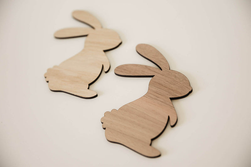 Zwei Osterhasen aus Holz liegend auf einem weißen TIsch