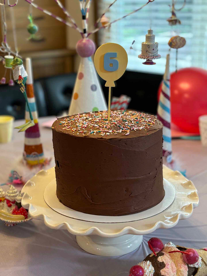 Acryl Ballon Caketopper auf einem Schokokuchen auf einem Geburtstagstisch, gelb mit einem blauen sechs