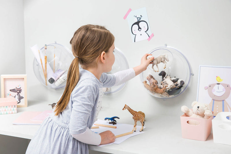 Ein Mädchen im Kinderzimmer spielt am Tisch mit Tieren, sie tut ein Pferd zurück in einer Wandkugel aus Kunststoff, was an der Wand hängt