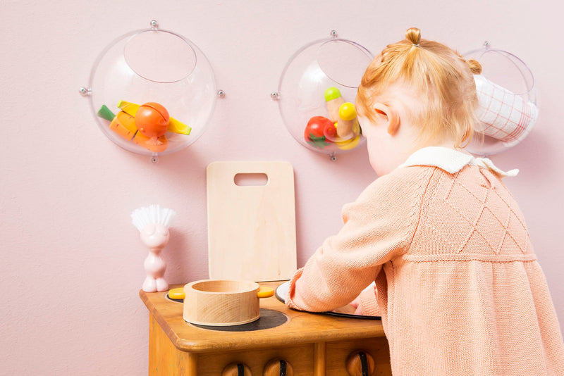 Eine Spielküche im Kinderzimmer. Drei Wandkugeln aus Kunststoff hängen an der rosa Wand. Ein Mädchen spielt.