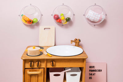 Eine Spielküche im Kinderzimmer. Drei Wandkugeln aus Kunststoff hängen an der rosa Wand.
