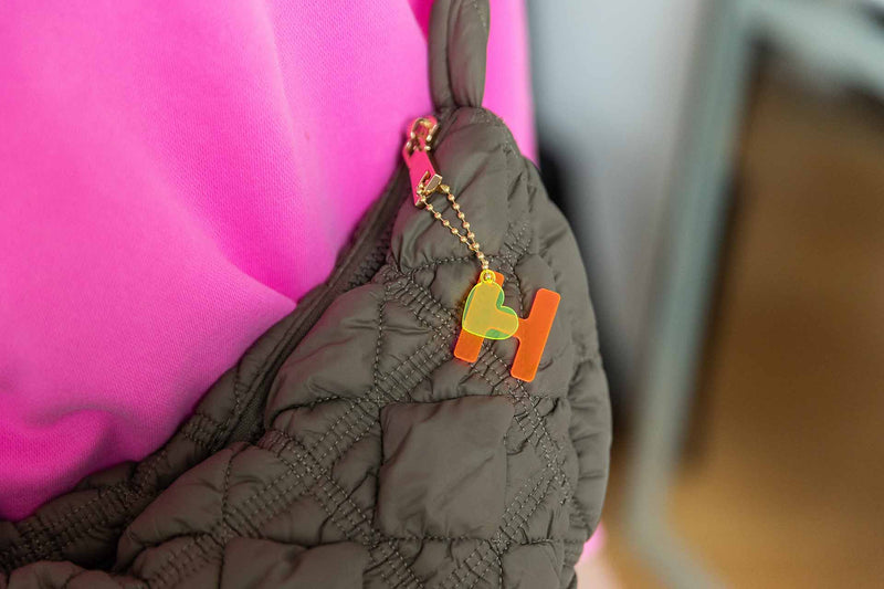 Ein Acryl Neon rosa H und gelbes Herz Anhänger auf eine goldene Kette hängen an einer Handtasche