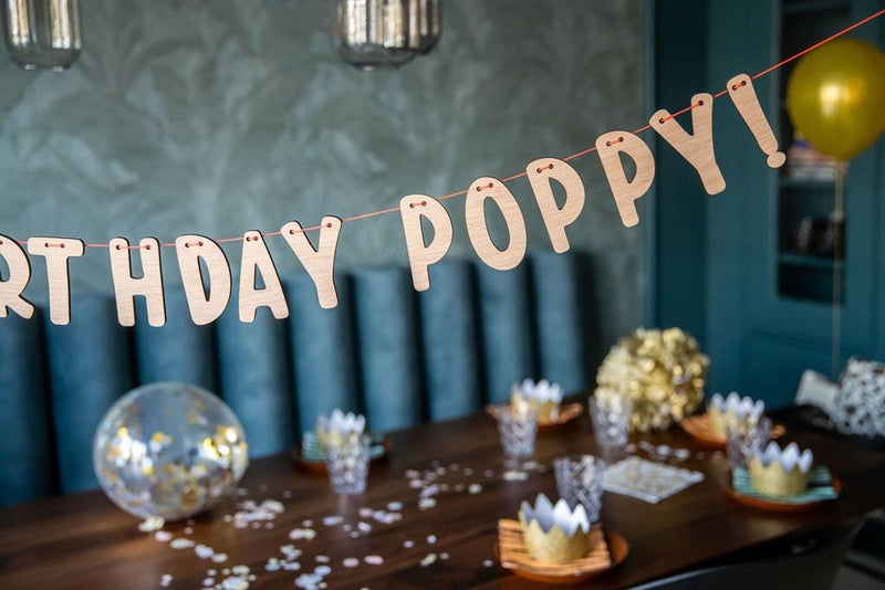Happy Birthday Girlande + dein Name personalisiert mit den Namen Poppy. Schön dekorierten Tisch im Hintergrund.