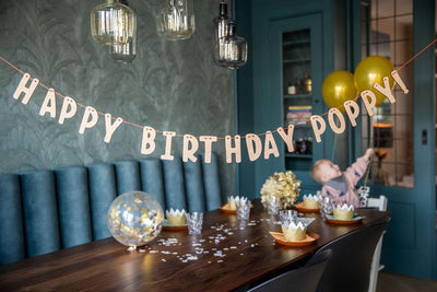 Happy Birthday Girlande + dein Name personalisiert mit den Namen  Poppy. Schön gedeckten Geburtstagstisch im Hintergrund. Kind am Tisch.