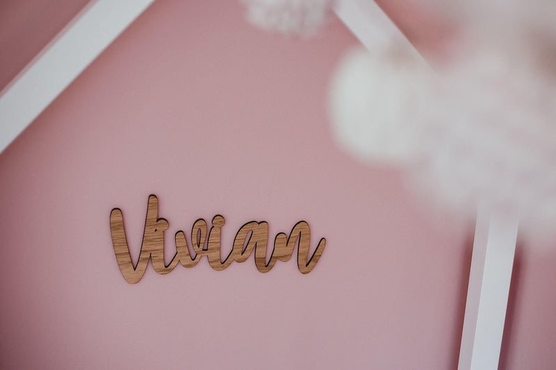 Namensschild aus Holz "Vivian" auf einer pinken Wand im Kinderzimmer