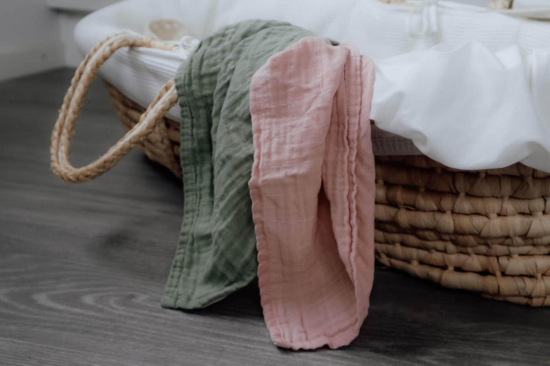 Zwei Mulltücher - grün und rosa - in einem Babykorb.