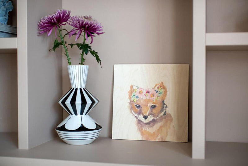Waldwunder Fuchs Kunstdruck auf Holz in einem Regal neben einer Vase mit Blumen. 